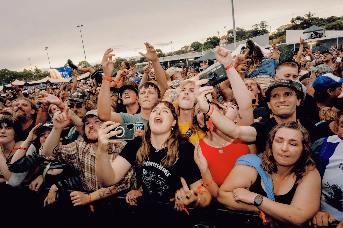 The front row at Nice Day To Go To The Club, hands up and singing along against the barrier, with a crowd-surfer going over behind them